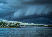 A storm cloud nears the Florida coast as boats sail on the water near homes.