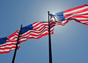 Three American flags blow in the wind against a blue, sunny sky. 