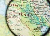 A magnifying glass above a map focuses on the country of Iraq
