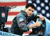 Tom Cruise as Maverick gives a thumbs up while sitting in an open fighter jet cockpit.